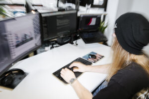 Schreibtisch mit Bildschirmen und Laptop und ein Mensch der mit einem Stuhl dran sitzt