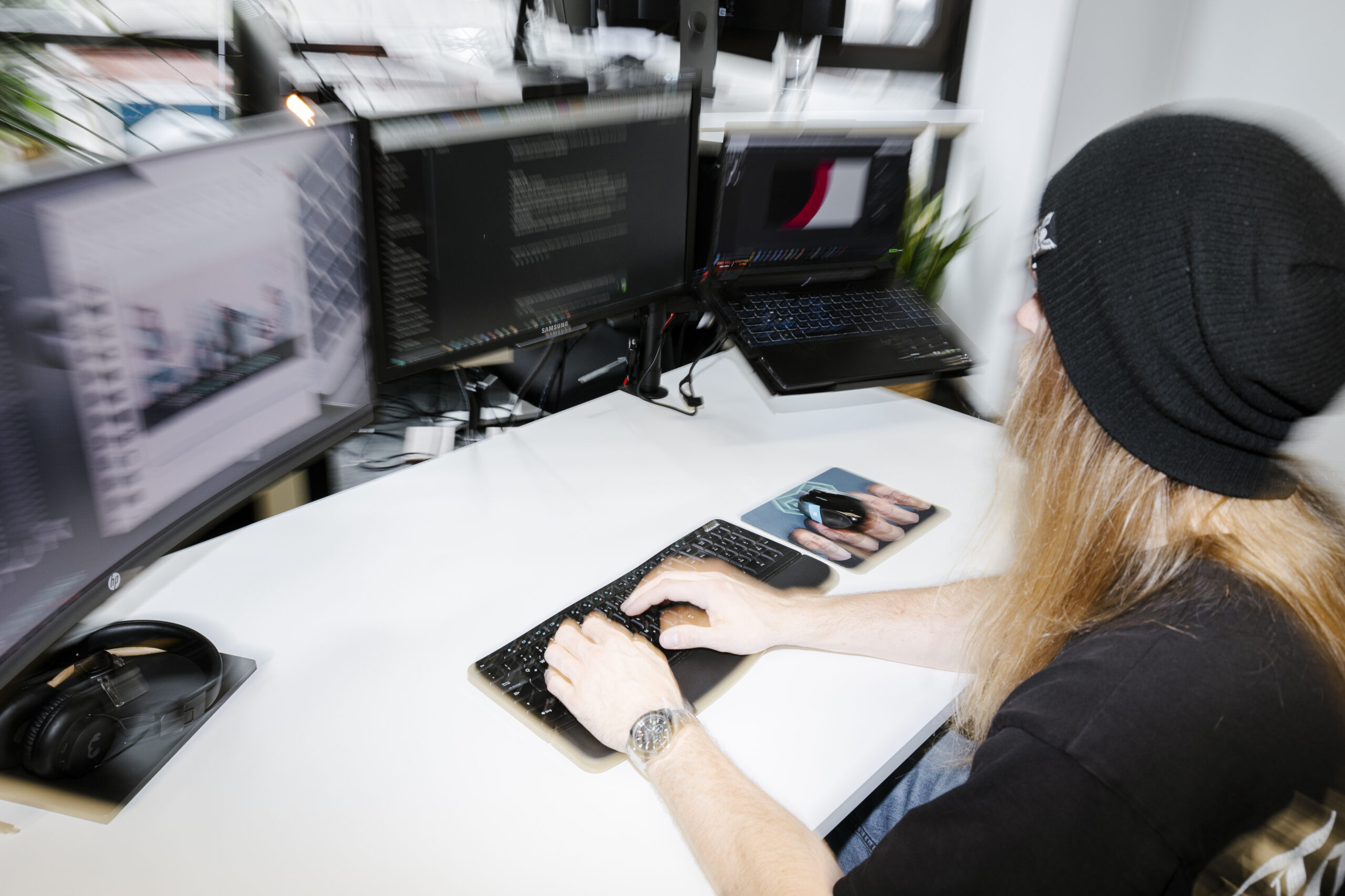 Schreibtisch mit Bildschirmen und Laptop und ein Mensch der mit einem Stuhl dran sitzt