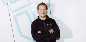 Ein Mann steht vor einer weißen Wand und an der Wand klebt eine Eule