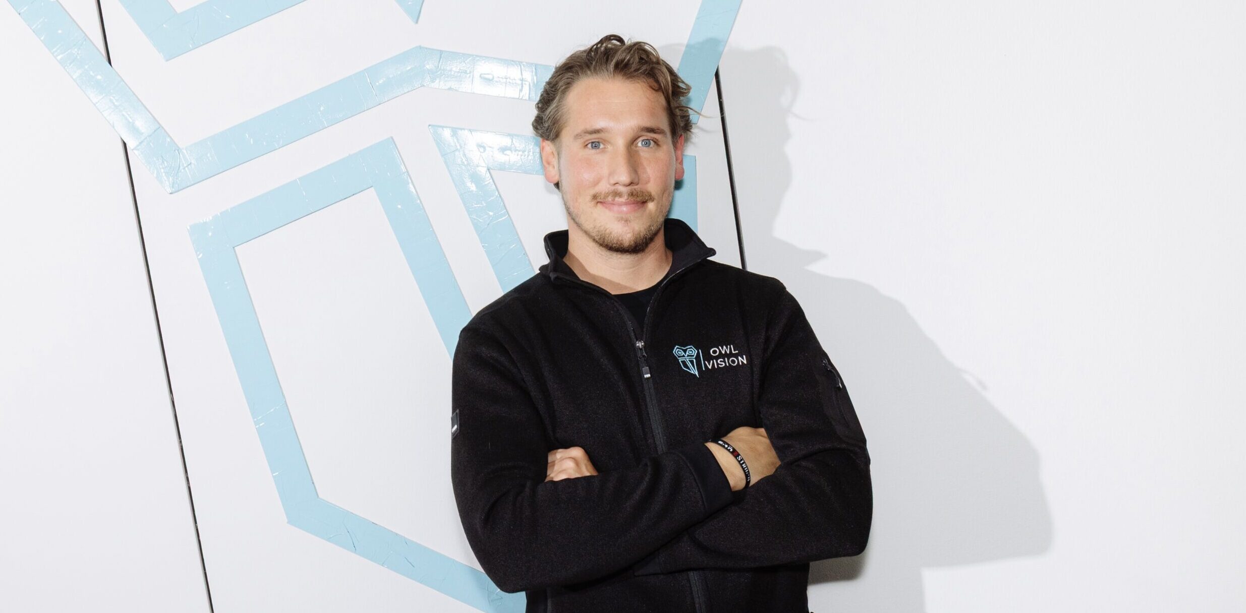 Ein Mann steht vor einer weißen Wand und an der Wand klebt eine Eule